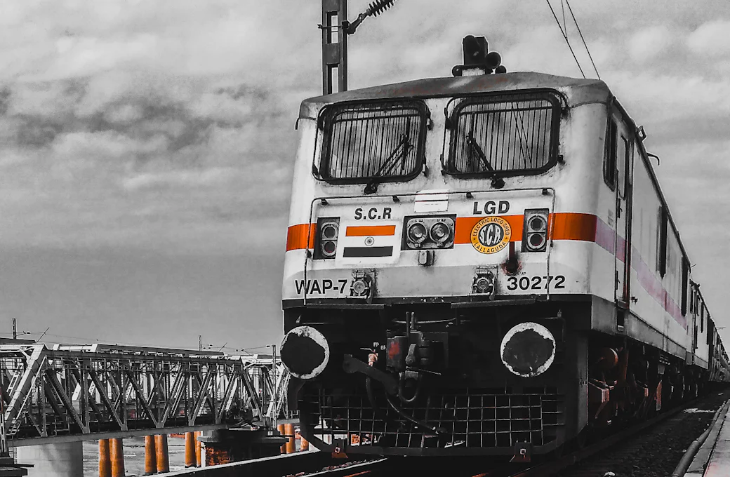 Indian Railways WAP-7 electric locomotive on the tracks with overhead lines and a steel bridge